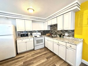 A kitchen with white cabinets, a microwave, a stove, and a tiled backsplash. - 1 bdrm:beach across st, Port  8 mi, Ron Jon’s 4 mi (Cocoa Beach)