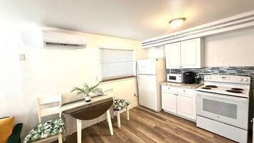 A compact kitchen with a dining area, white cabinetry, a microwave, a stove, and a refrigerator.