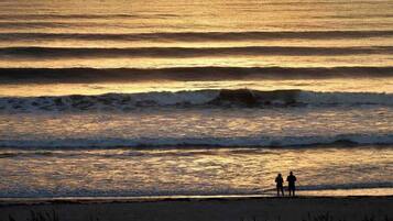 A beach scene with waves and two people standing on the shore.