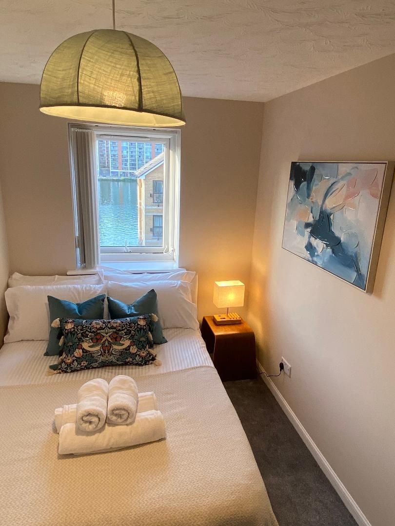 A hotel room with a bed, a bedside lamp, a window, and a painting on the wall.