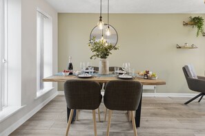 Un coin repas avec une table en bois, deux chaises, un vase de fleurs et une bouteille de vin.