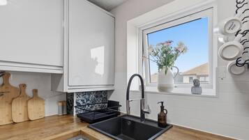 A modern kitchen with a black sink, wooden cutting boards, a window with a view, and a cactus on the windowsill.
