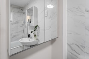 Une salle de bain avec un lavabo en marbre blanc, une douchette à main et une plante en pot.