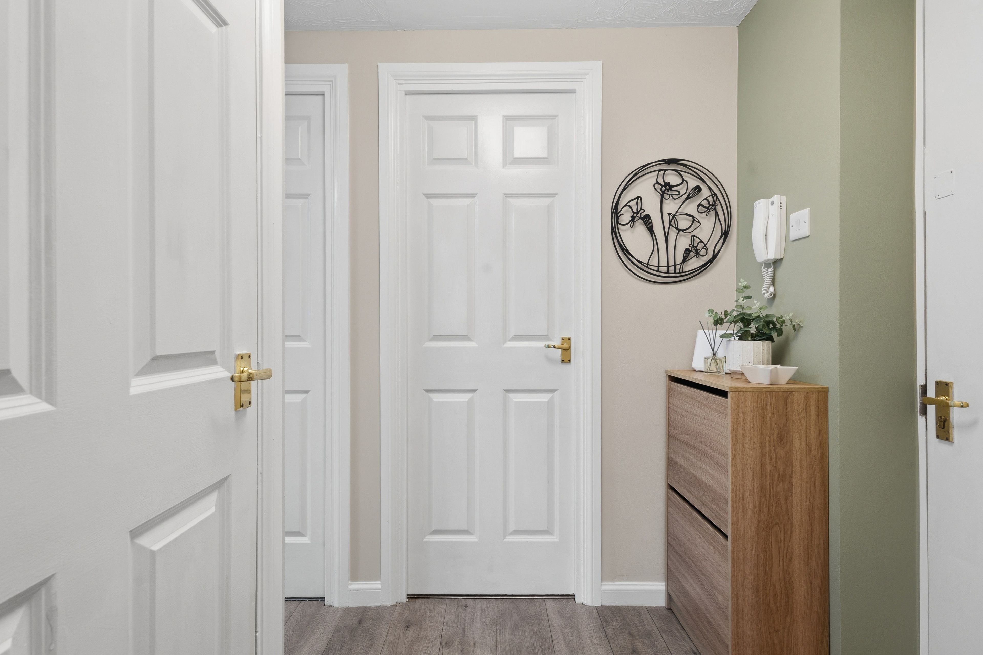A hallway with a white door, a wooden cabinet, and a wall-mounted telephone.