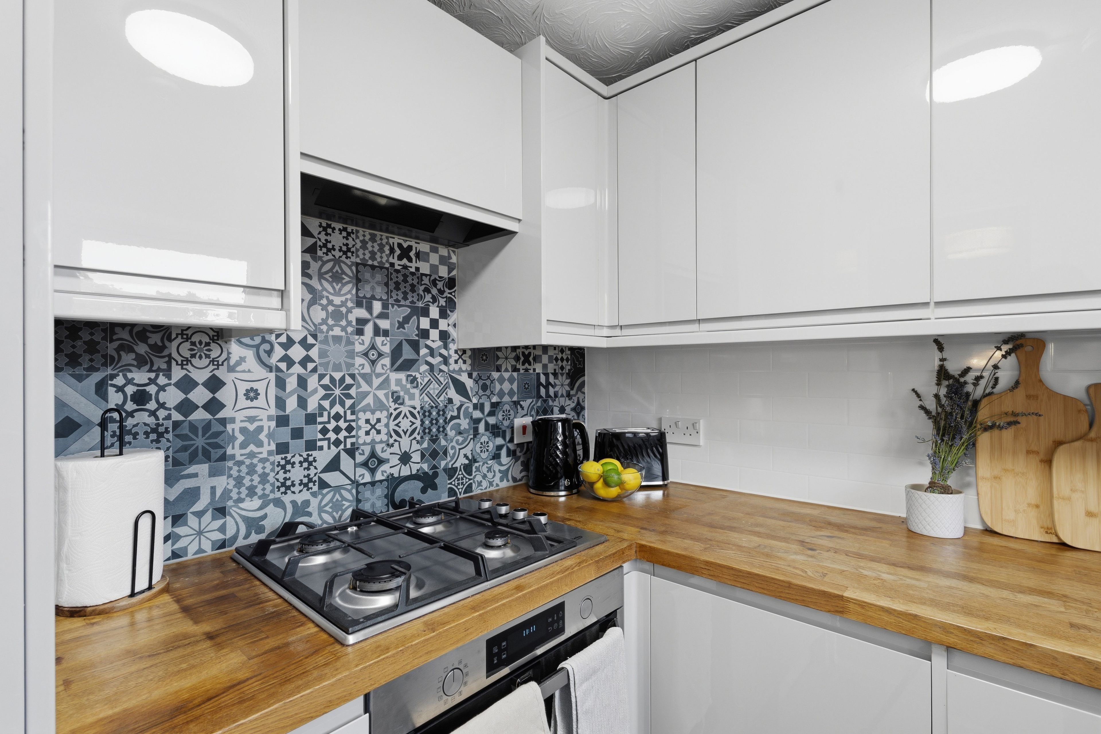 A modern kitchen with white cabinets, a patterned backsplash, and a wooden countertop.