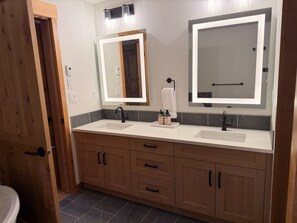 A bathroom with two sinks, a mirror, and wooden cabinets. - New | Modern Mountain Retreat | Walk to Town (Canmore)