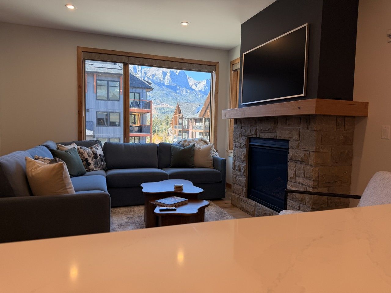 A modern living room with a stone fireplace, a large flat-screen TV, and a sofa with cushions.
