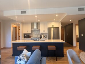 A modern kitchen with a central island, bar stools, and a seating area with a sofa and chairs. - New | Modern Mountain Retreat | Walk to Town (Canmore)