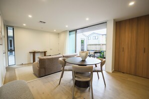 Un espace de vie moderne comprenant un canapé, une table à manger et des chaises. Une grande fenêtre offre une vue sur l’extérieur.