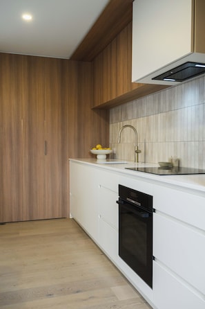 Een moderne keuken met houten kastjes, een wit aanrecht, een ingebouwde oven en een roestvrijstalen spoelbak.