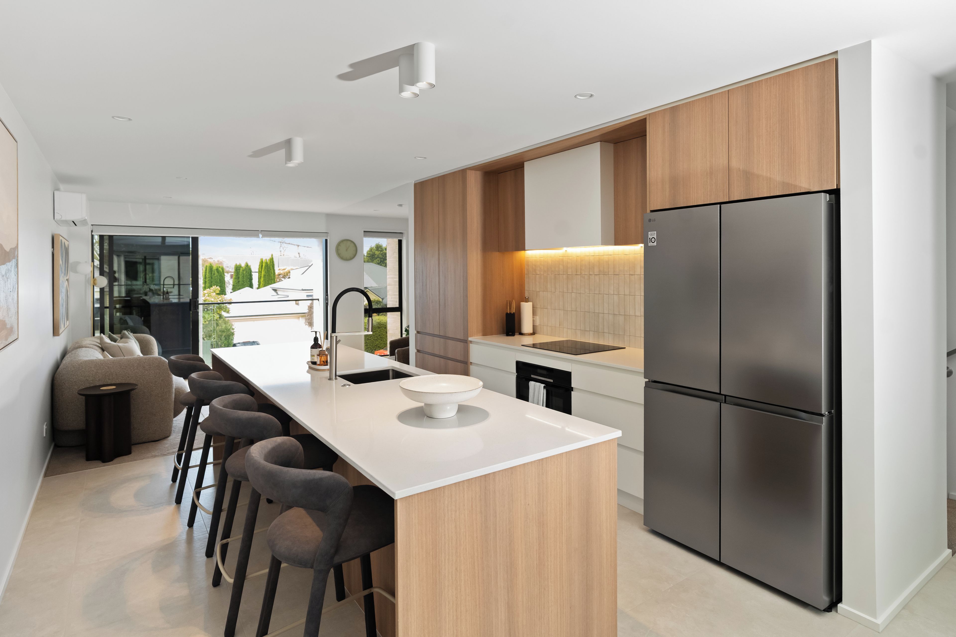 A modern kitchen with a central island, bar stools, a stainless steel refrigerator, and wooden cabinetry.