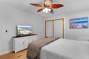 Ein Schlafzimmer mit einem Bett, einem Fernseher auf einer Kommode, einem Deckenventilator und einem Bild an der Wand.