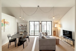 A modern living room with a dining area, a sofa, a TV, and a large window. - Bairro Alto Modern W Terrace AND Garage by Homing (Lisbon)