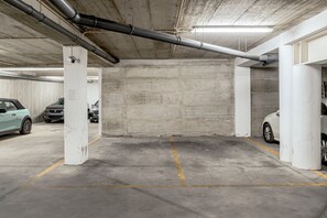 A parking garage with concrete pillars, overhead pipes, and marked parking spaces. - Bairro Alto Modern W Terrace AND Garage by Homing (Lisbon)