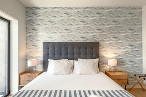 A hotel room with a large bed, two bedside lamps, a grey upholstered headboard, and a patterned wallpaper. - Bairro Alto Modern W Terrace AND Garage by Homing (Lisbon)