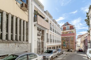 Straßenansicht mit parkenden Autos, einem Gebäude mit moderner Fassade und einem Wandgemälde.
