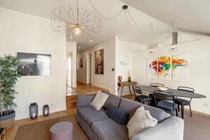 Ein modernes Wohnzimmer mit einem grauen Sofa, einem Esstisch und einem farbenfrohen abstrakten Gemälde.