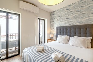 A hotel room with a bed, a nightstand, a lamp, a view through a sliding door, and a textured wall. - Bairro Alto Modern W Terrace AND Garage by Homing (Lisbon)