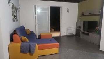 Sala de estar com sofá, televisão e porta de vidro deslizante que dá para uma área externa.