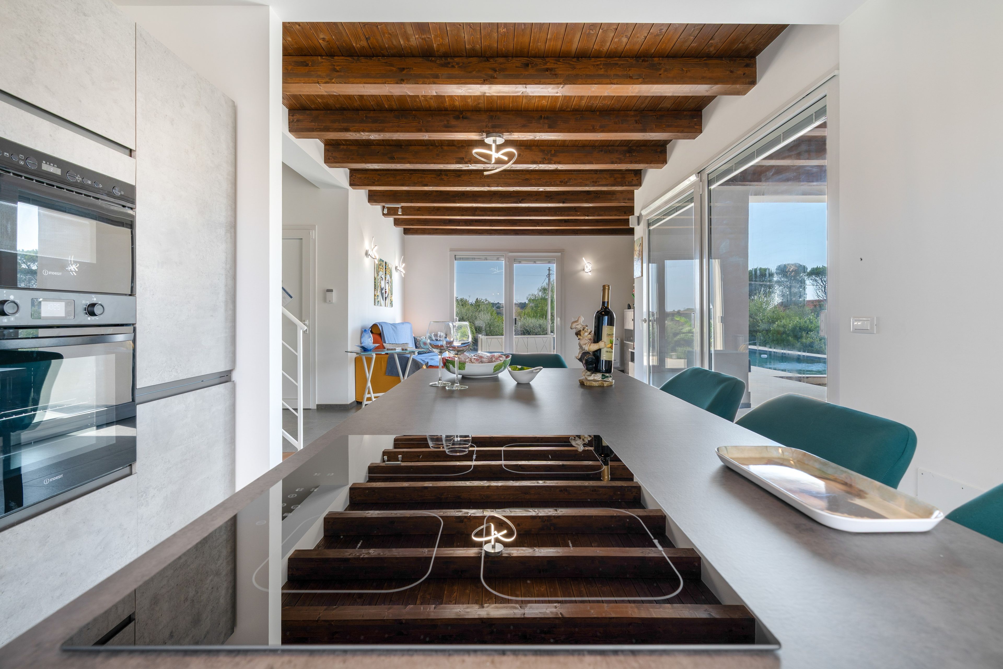 A modern kitchen with a wooden ceiling, built-in appliances, and a dining area with a view.