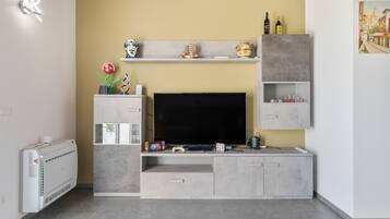 Un soggiorno moderno con televisione a schermo piatto, console per videogiochi e una pianta decorativa.