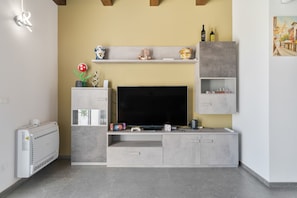 A modern living room with a flat-screen TV, gaming consoles, and a decorative plant.