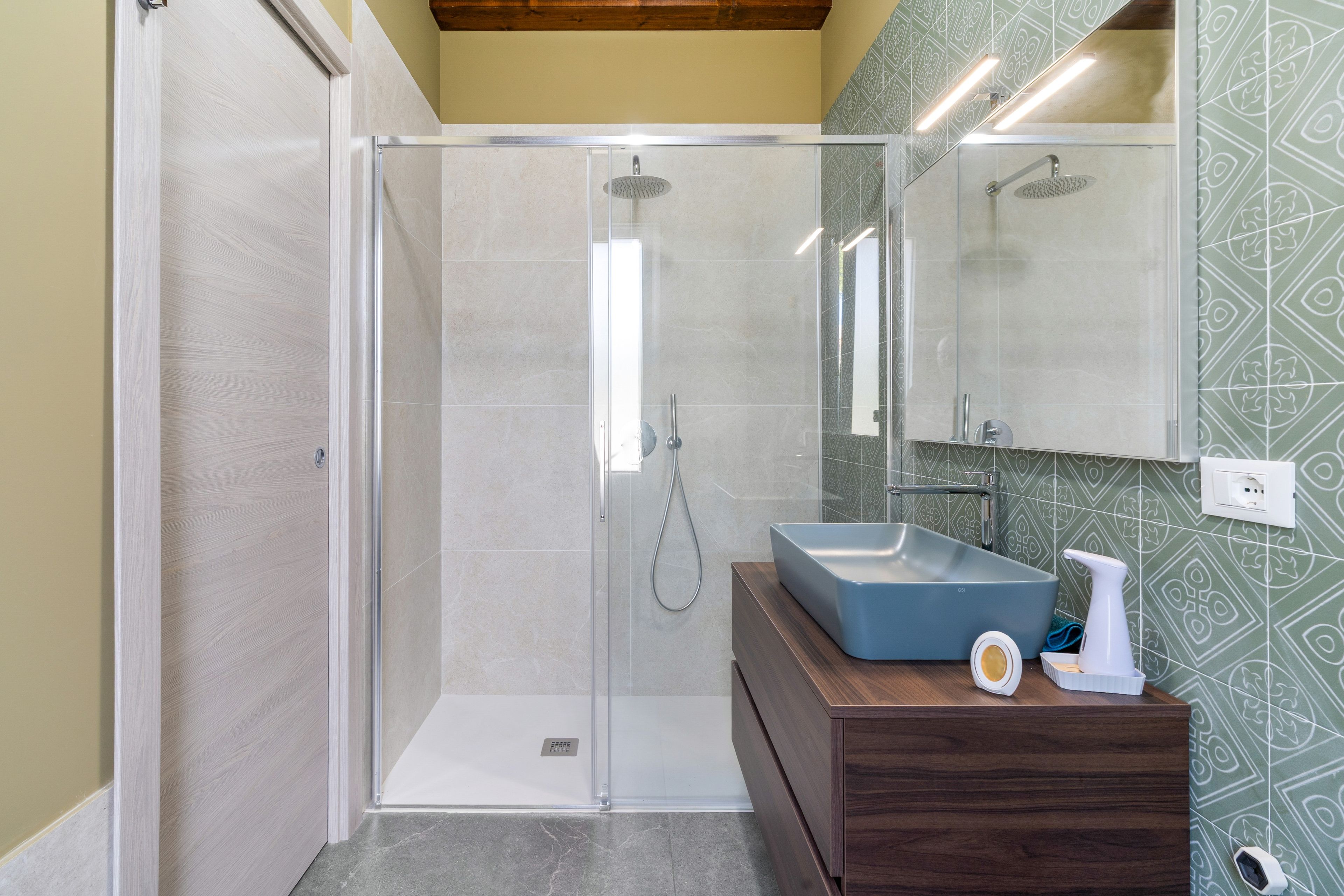 A modern bathroom with a glass-enclosed shower, a wooden vanity, and a patterned wall.