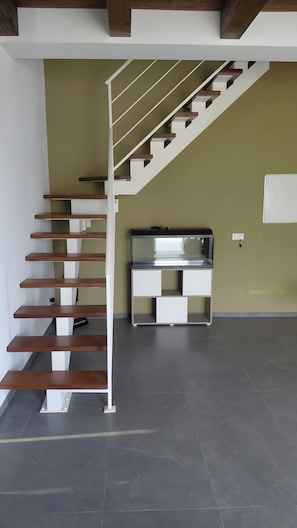 Una escalera con escalones de madera y barandillas blancas, que lleva a un rellano con una consola blanca y un televisor montado en la pared.