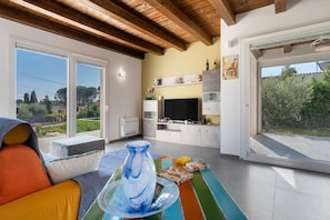 A modern living room with a large TV, a dining table, and a view of the outdoors.