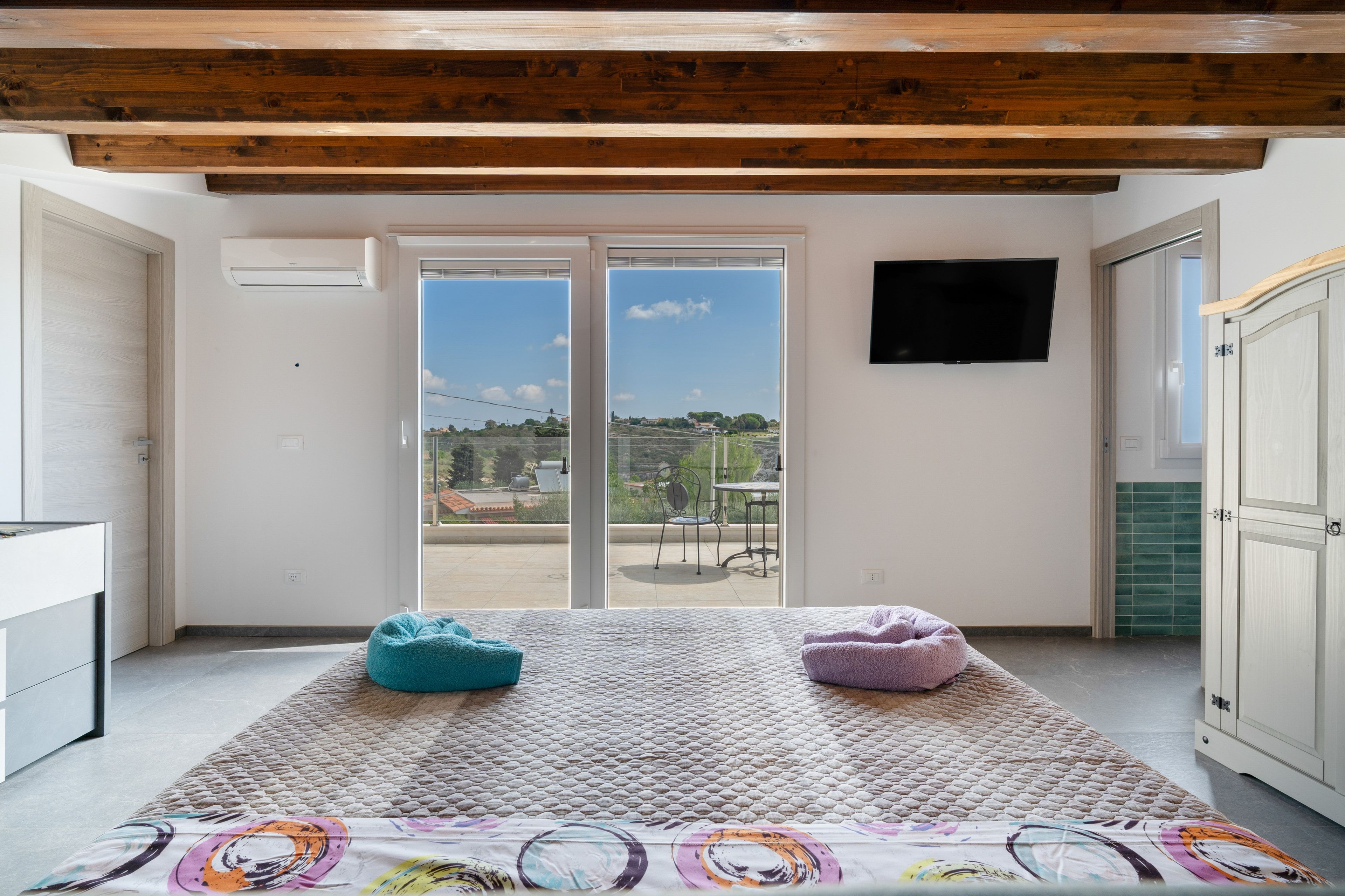 A room with a large sliding glass door leading to an outdoor area, a flat-screen TV mounted on the wall, and a bed with a patterned bedspread.