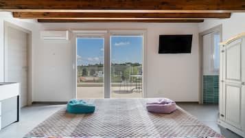 A room with a large sliding glass door leading to an outdoor area, a flat-screen TV mounted on the wall, and a bed with a patterned bedspread.