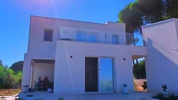 Une maison moderne à deux étages, dotée d’un toit plat, de grandes fenêtres et d’un vaste porche à l’avant.