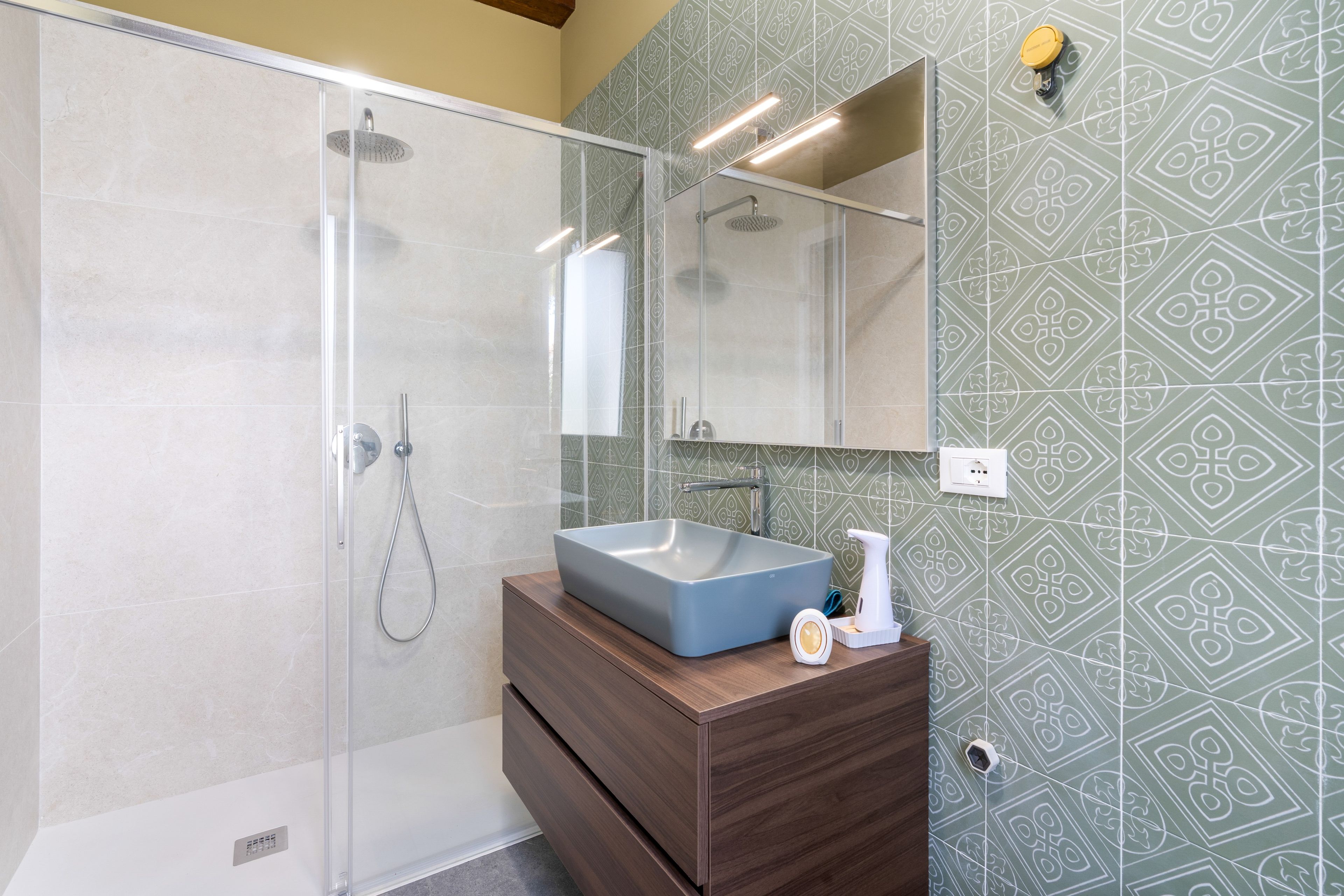 Ein modernes Badezimmer mit einer gläsernen Duschkabine, einem hölzernen Waschtisch und Wandfliesen mit Muster.