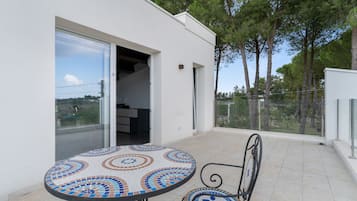 Une terrasse extérieure moderne, avec une table et des chaises carrelées, une porte-fenêtre coulissante donnant sur une pièce, et une vue sur les arbres et un ciel dégagé.
