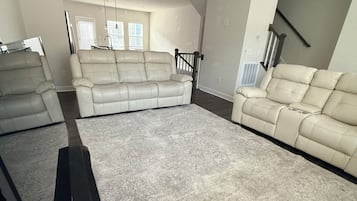 Un salón amplio con una alfombra grande color beige, dos sofás color beige, un ventilador de techo y una escalera.