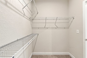 Een hoek van een kamer met een witte deur, een beige vloerkleed en twee metalen draadrekken tegen de muur.