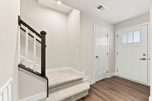 A clean, modern interior with a carpeted staircase, white walls, and wooden flooring.