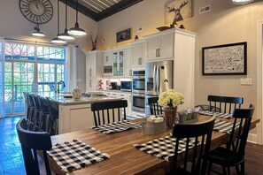 A modern kitchen with white cabinets, stainless steel appliances, and a dining area with a wooden table and chairs. - Norris Lake Cabin with Deck, Dock & Playground (Sharps Chapel)