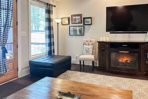 A living room with a fireplace, a television, and a window with curtains. - Norris Lake Cabin with Deck, Dock & Playground (Sharps Chapel)