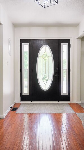 A black double door with a diamond-shaped window, a doormat, and a wooden floor. - The Summer House - Lake Access - Hot Tub & Kayaks (Lambton Shores)