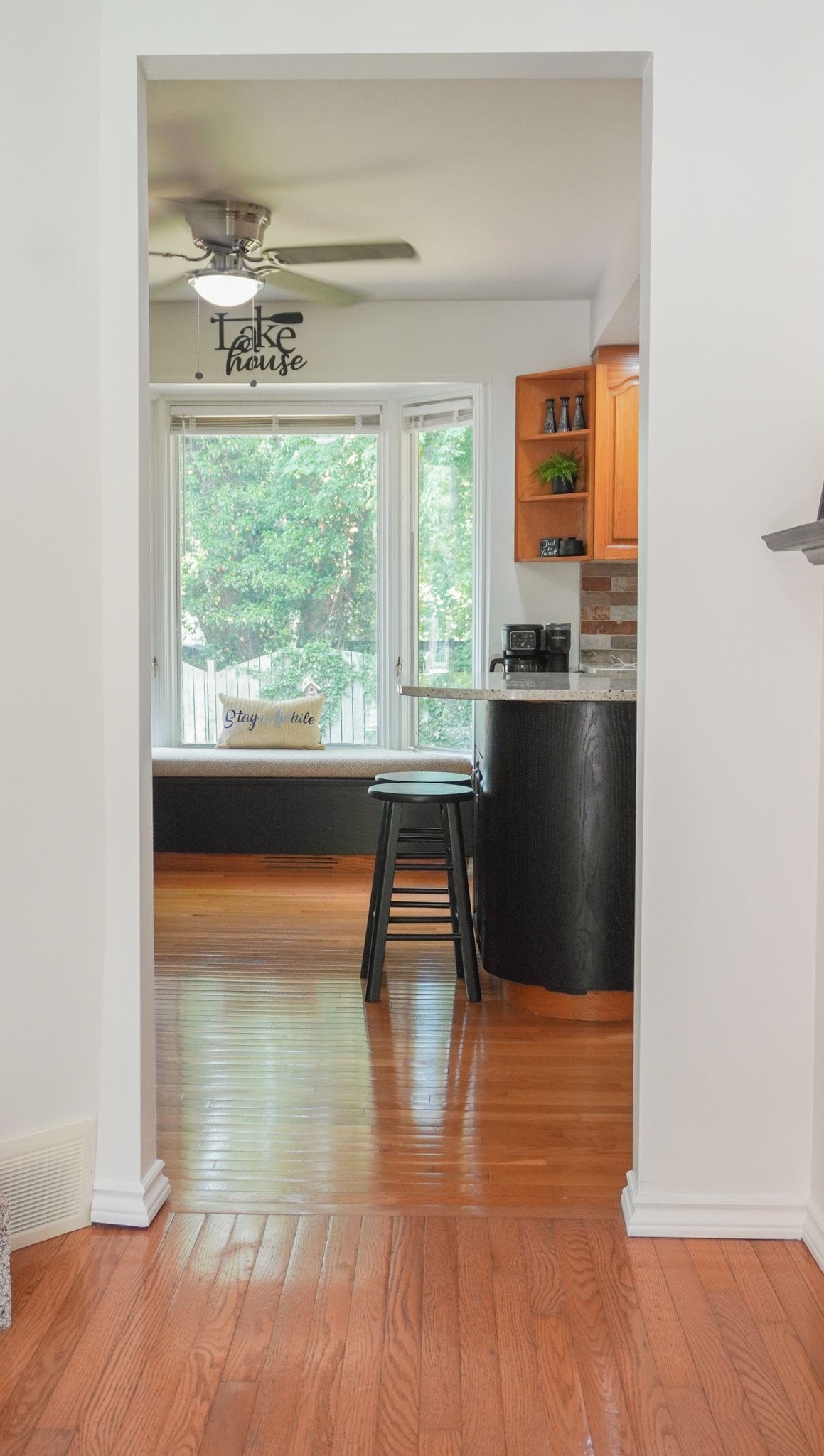 A kitchen with a window seat, wooden flooring, and a ceiling fan.