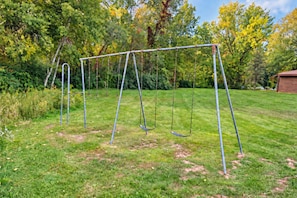 Ein Metall-Schaukelstuhl in einem grasbewachsenen Garten mit Bäumen im Hintergrund.