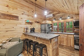 Ein rustikales Blockhaus mit Küchenbereich, Holzwänden, einer Bar mit Hockern und einem Schild mit der Aufschrift 'RED LOG RIVER LODGE'.