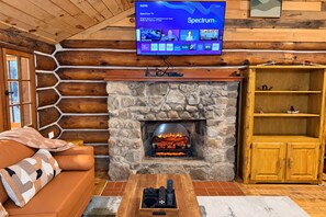 Ein gemütliches Wohnzimmer mit Kamin aus Stein, einem darüber montierten Fernseher und einem hölzernen Bücherregal.