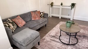 A grey sofa with striped cushions, a round coffee table, and a patterned rug in a room with wooden flooring and a white radiator. - Stylish 2-Bedroom Flat in South London | Sleeps 4 (London)