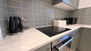 A kitchen with a black induction cooktop, a coffee maker, and a toaster. - Stylish 2-Bedroom Flat in South London | Sleeps 4 (London)