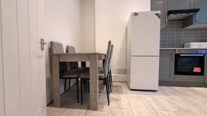 A modern kitchen with a built-in oven, a refrigerator, and a dining area with a table and chairs. - Stylish 2-Bedroom Flat in South London | Sleeps 4 (London)