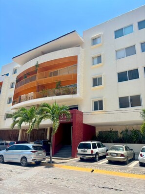 A multi-story building with a curved facade, a red entrance, and a parking area with several cars. - Excellent location (Puerto Vallarta)