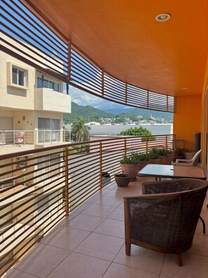 A balcony with a view of a beach and mountains, furnished with wicker chairs and a table. - Excellent location (Puerto Vallarta)