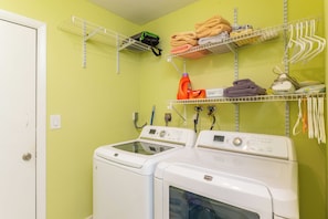 A laundry area with two front-loading washing machines, shelves with folded towels and a laundry basket, and a power outlet on the wall. - Relaxed Retreat with Porch Dining and Yard (Lighthouse Point)